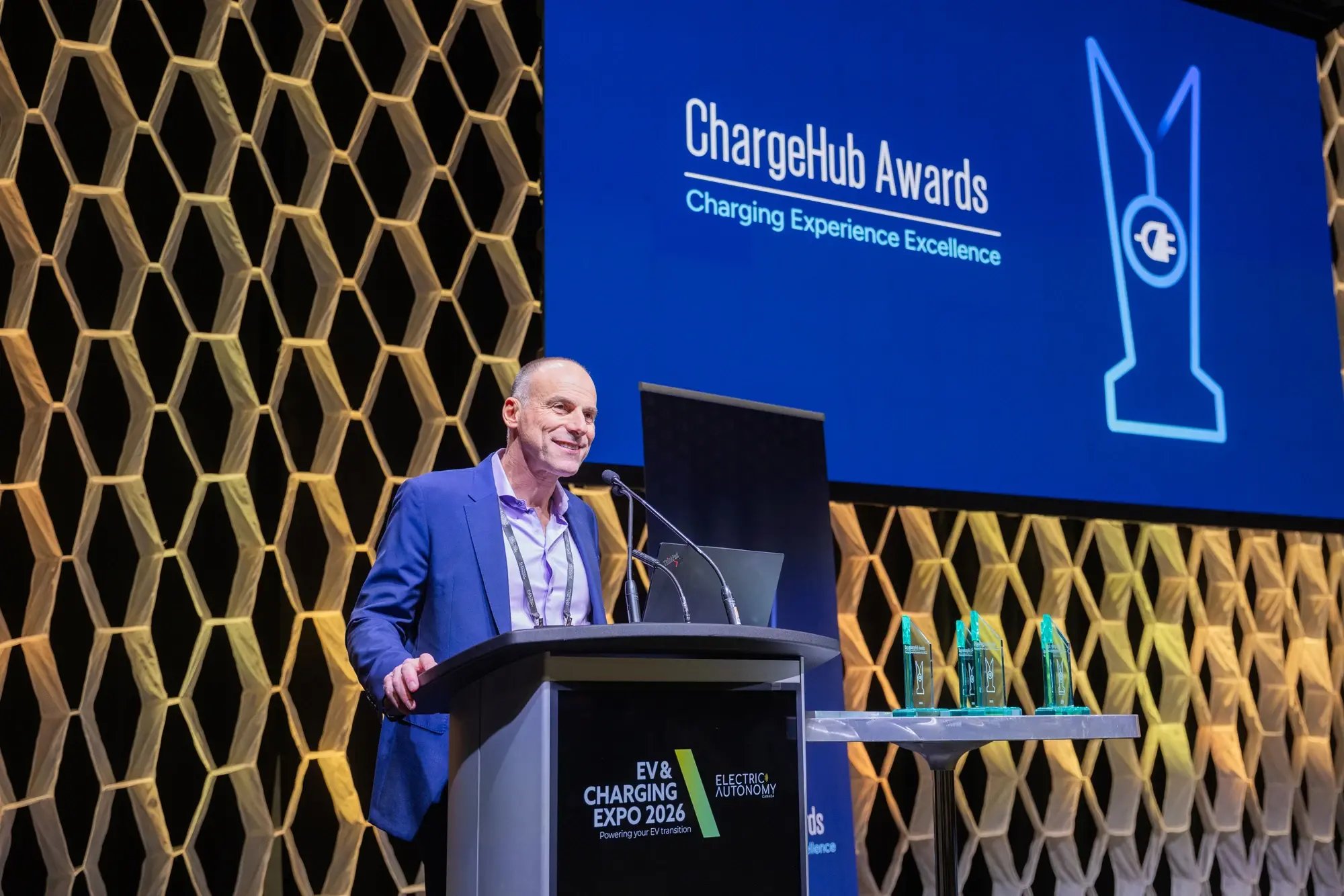 Nino Di Cara speaking at the podium during the ChargeHub Awards ceremony beside the trophies.