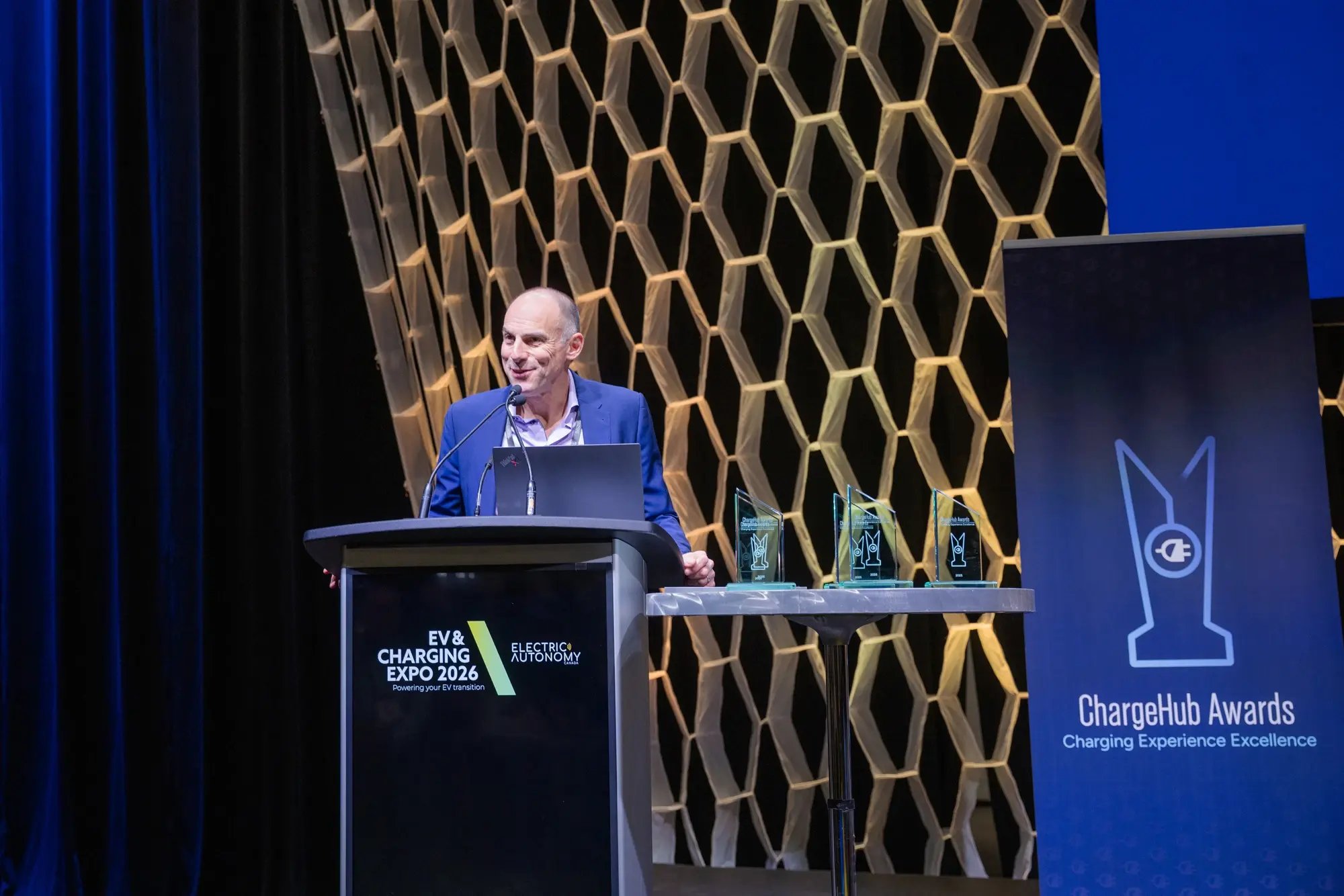 Nino Di Cara addressing attendees at the ChargeHub Awards ceremony with trophies on display.