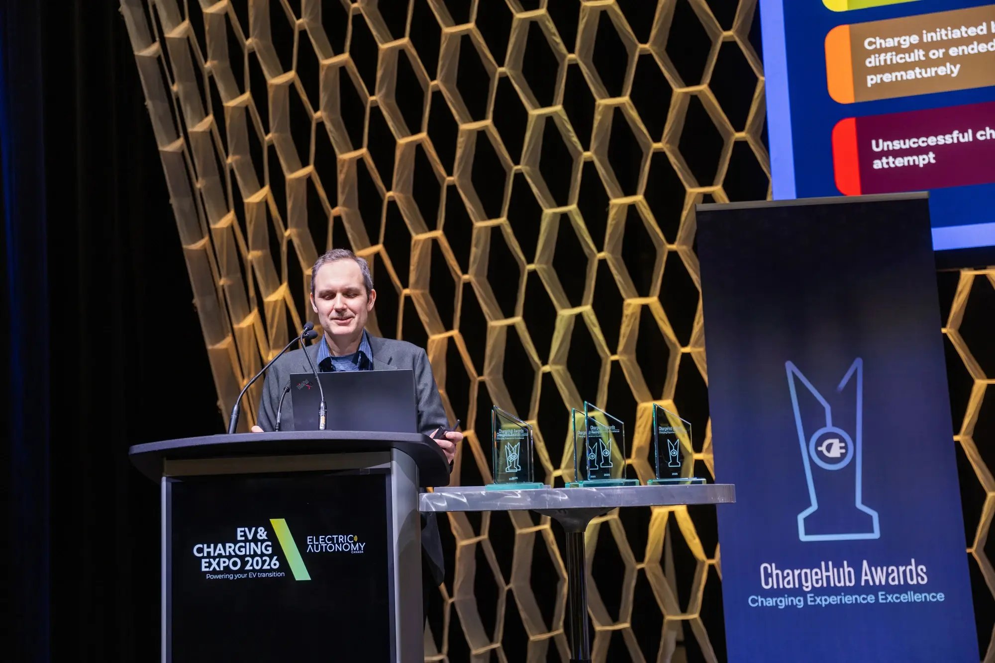 Simon Ouellette speaking at the ChargeHub Awards ceremony with trophies and presentation screen beside the podium.