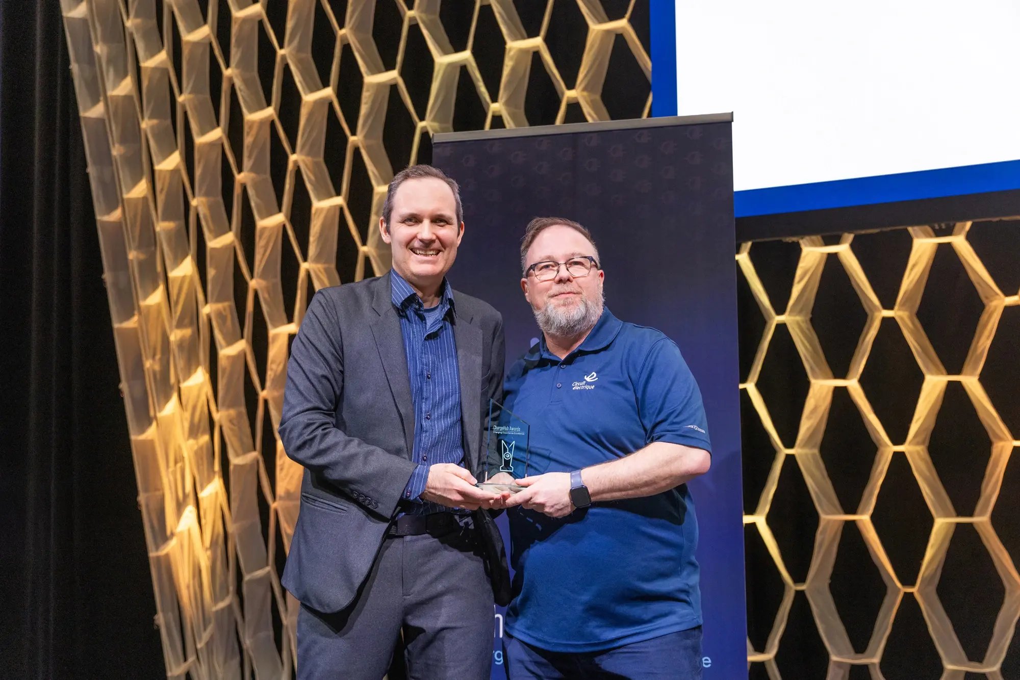 Simon Ouellette and an award recipient posing with a ChargeHub Awards trophy on stage.