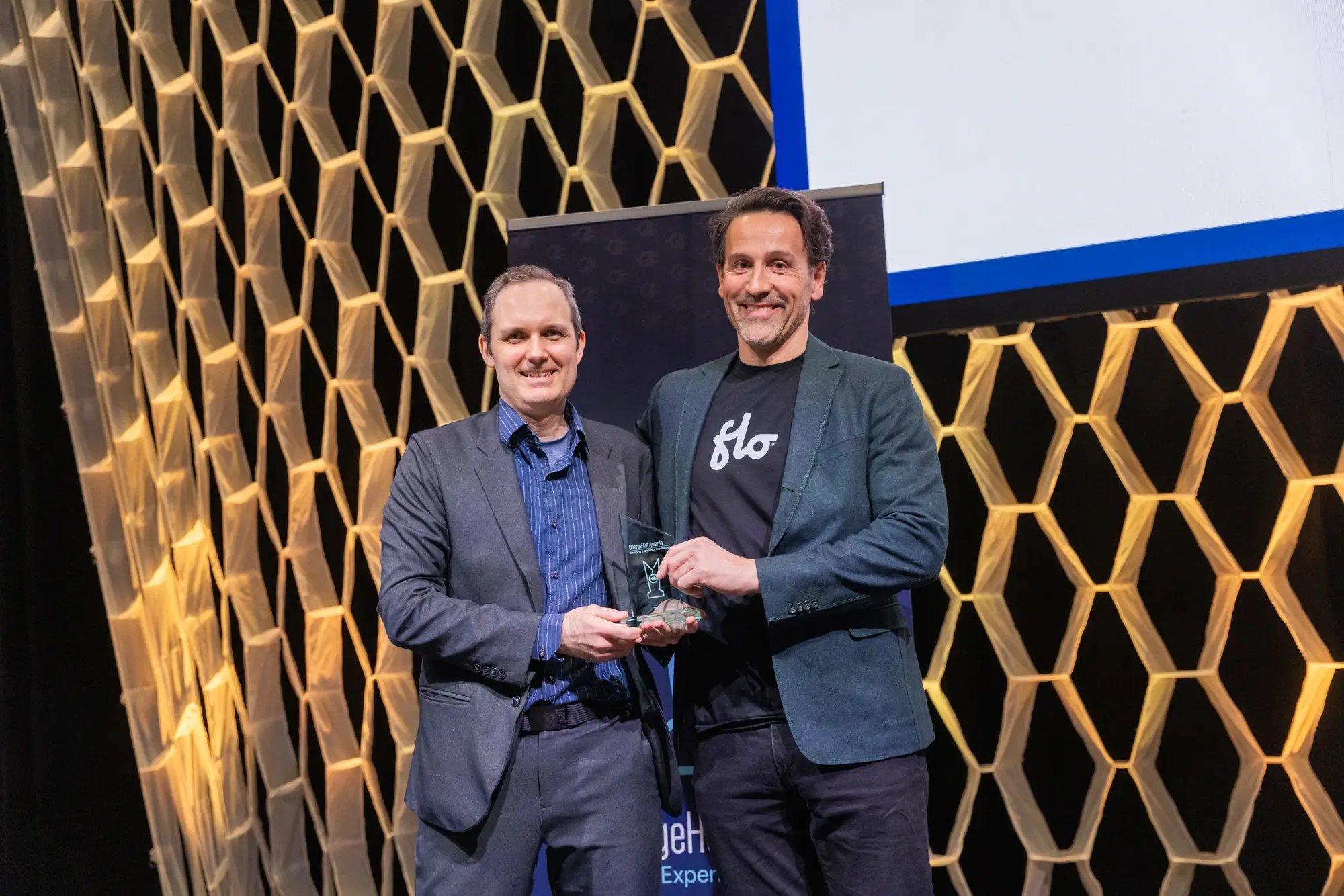 Simon Ouellette and a FLO representative holding a ChargeHub Awards trophy on stage.