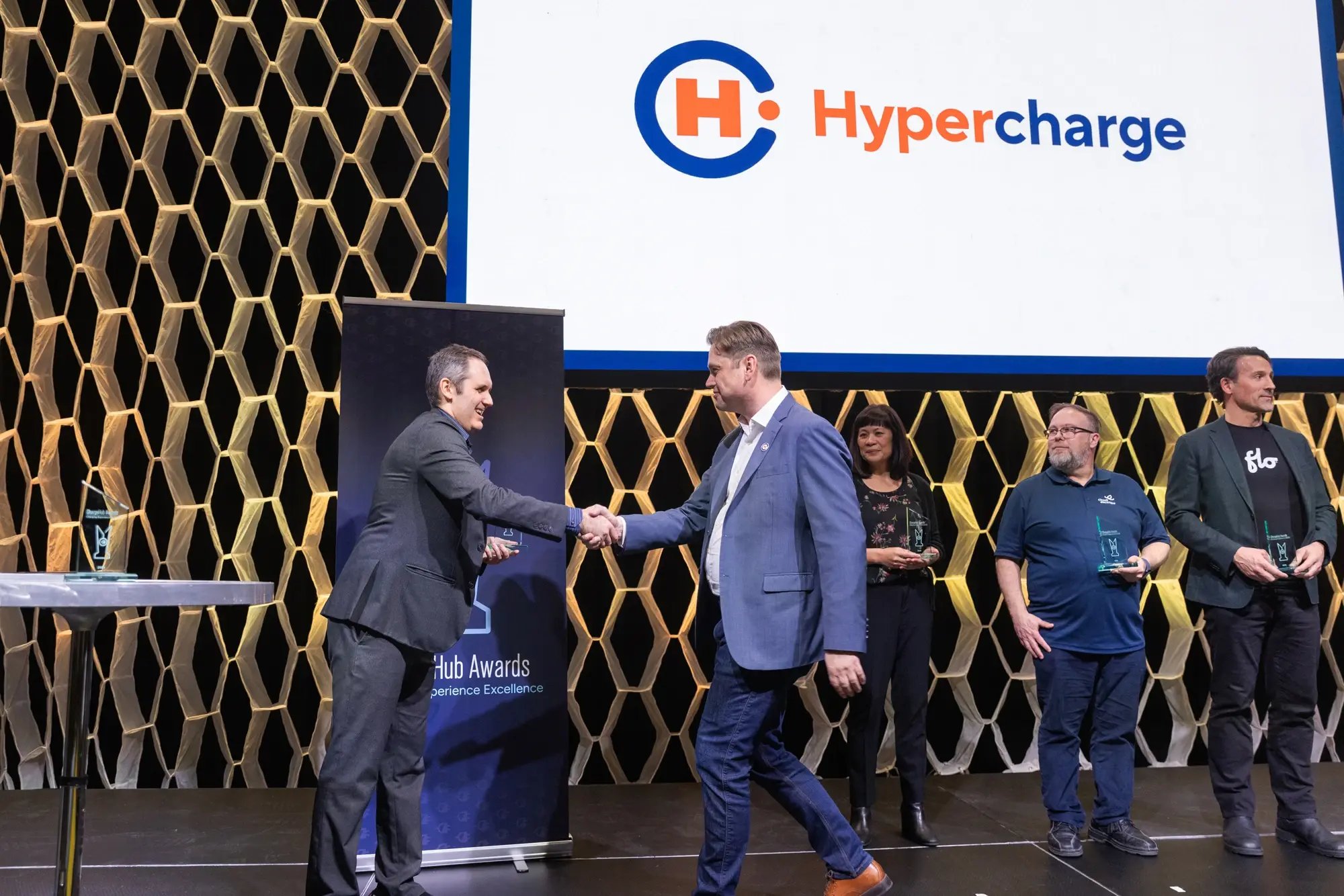 Simon Ouellette shakes hands with a recipient on stage as Hypercharge appears on screen at the ChargeHub Awards ceremony.
