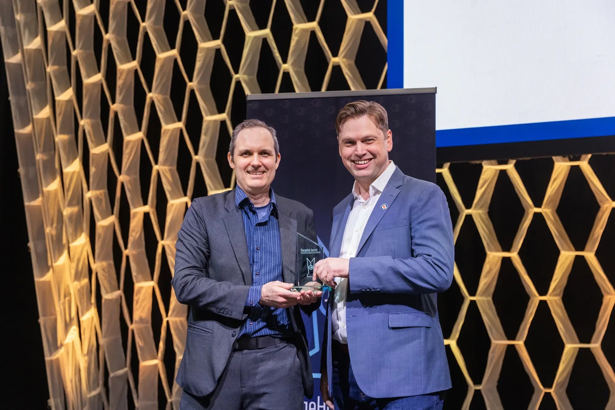 Simon Ouellette and an award recipient posing with a ChargeHub Awards trophy on stage.