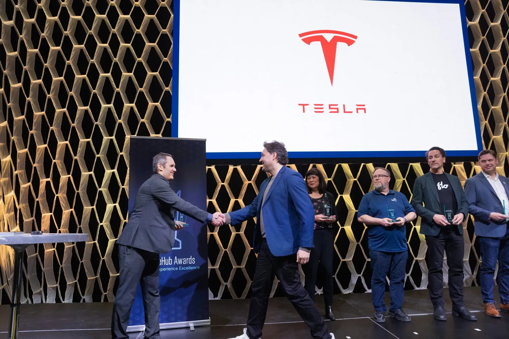 Simon Ouellette shakes hands with a recipient on stage as Tesla appears on screen at the ChargeHub Awards ceremony.