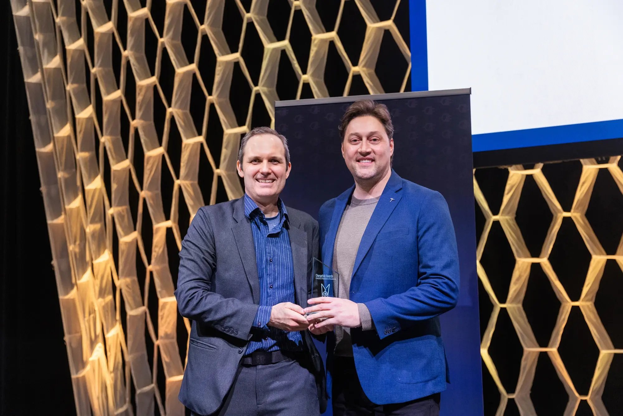 Simon Ouellette and a Tesla representative posing with a ChargeHub Awards trophy on stage.