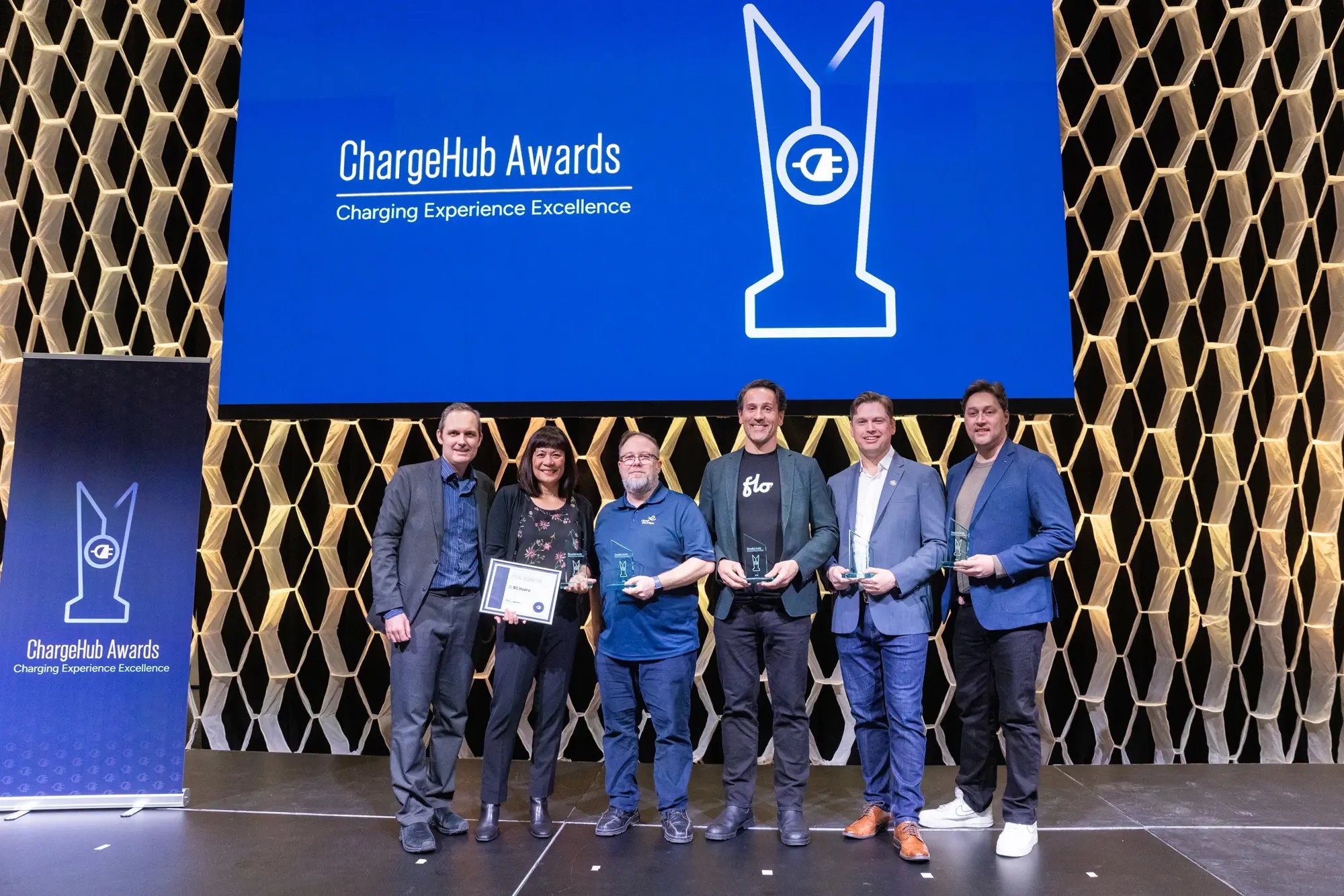 Group photo of ChargeHub Awards recipients holding trophies on stage beneath the event screen.