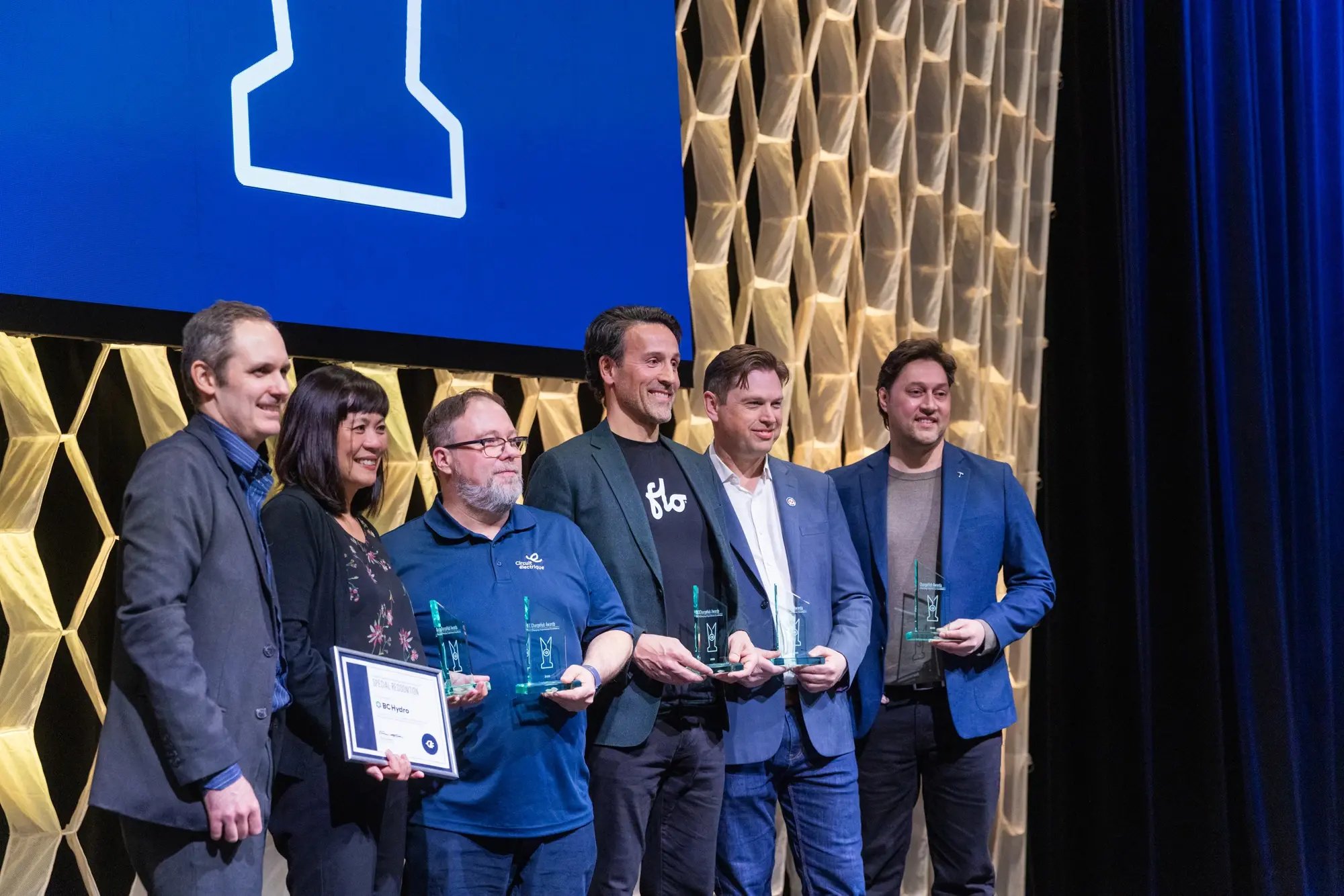 Side-angle group photo of ChargeHub Awards recipients holding trophies on stage.
