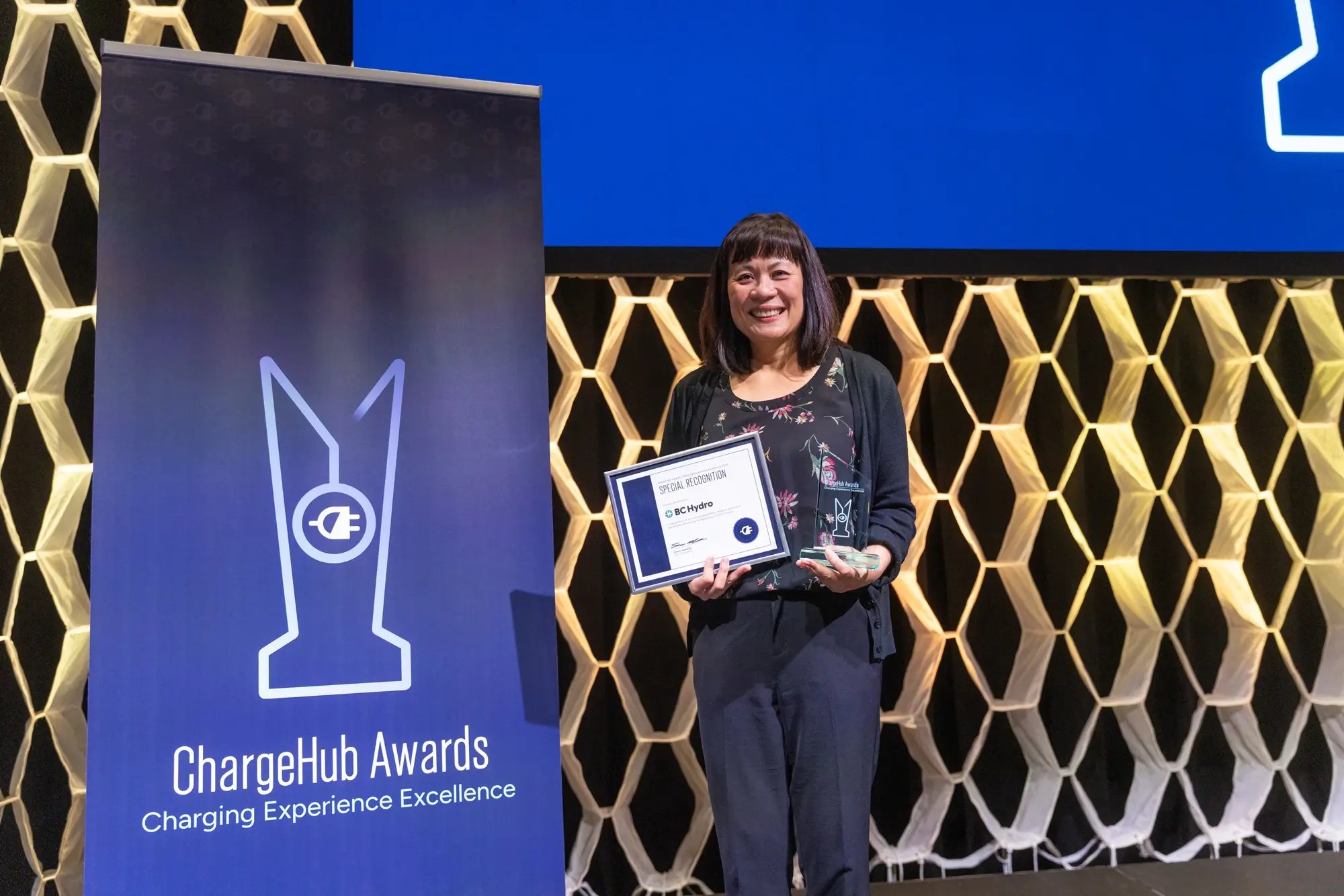 BC Hydro special recognition recipient holding a certificate and ChargeHub Awards trophy on stage.
