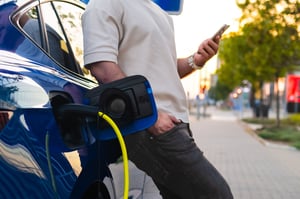 A driver using their phone while their electric car is charging at a public charging station
