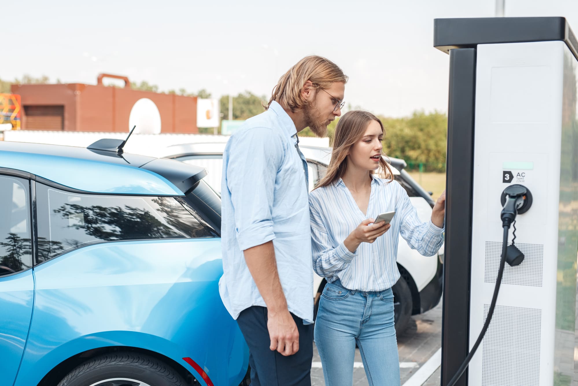 Couple charging an electric vehicle at a station using the ChargeHub app.